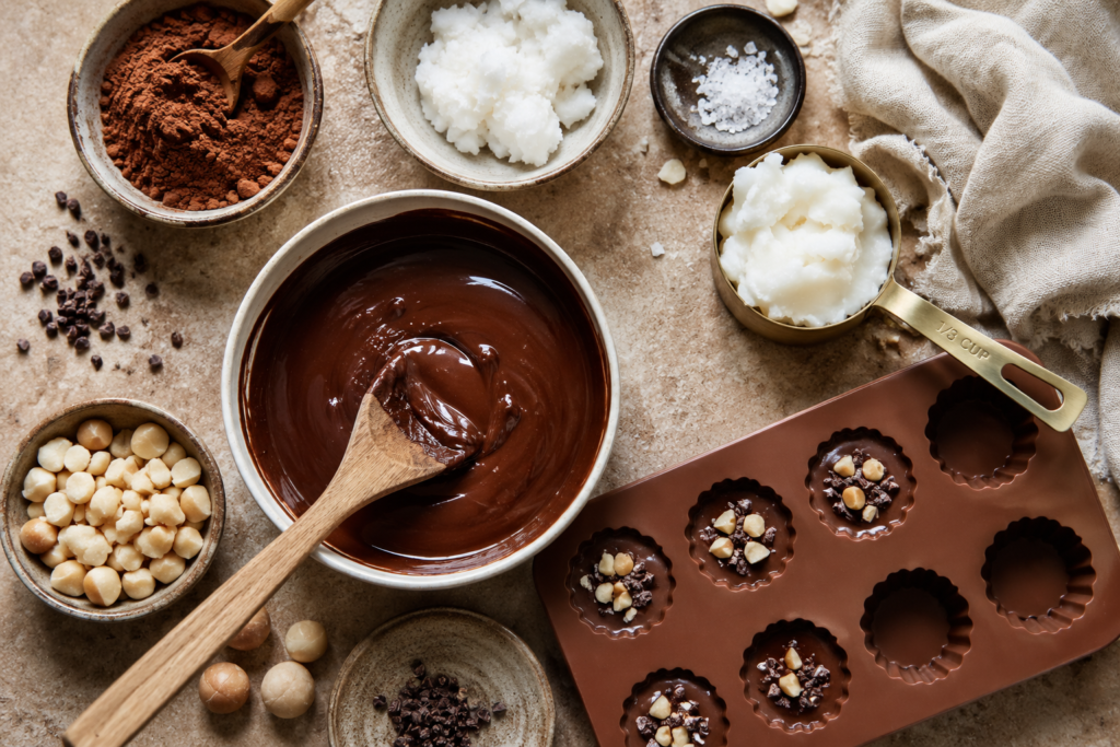 Coconut Chocolate Fat Bomb recipe preparation showcasing melted chocolate, cacao powder, coconut ingredients, macadamia nuts, and silicone molds on a warm artisan countertop, celebrating simple ingredients, rich flavor, and the ritual of homemade chocolate making.