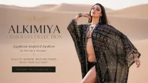 Model wearing the Alkimiya Obsidian Collection by Melodia Designs in a flowing black-and-gold Egyptian-inspired sheer kimono, posing in desert sand dunes beneath a soft neutral sky.