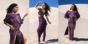 Model wearing a purple Karnak batwing top styled with a matching skirt and harem pants in a desert setting, showcasing geometric patterns and flowing movement.