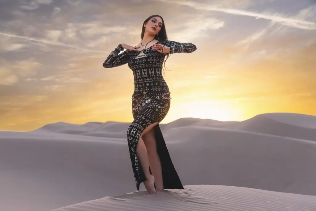 Woman wearing alkimiya nawal obsidian black sacred geometry dress posing on sand dunes at sunset