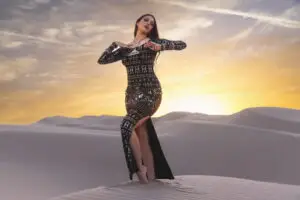 Woman wearing alkimiya nawal obsidian black sacred geometry dress posing on sand dunes at sunset