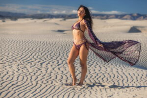 Woman wearing karnak zsazsa robe aubergine outfit with flowing scarf on white sand dunes