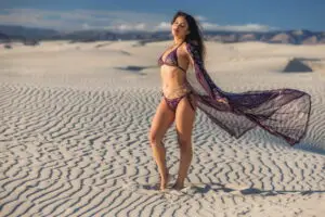 Woman wearing karnak zsazsa robe aubergine outfit with flowing scarf on white sand dunes